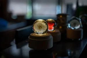 Nahaufnahme einer leuchtenden Löwenzahn-Glaskugel auf einer hölzernen Spieluhr
