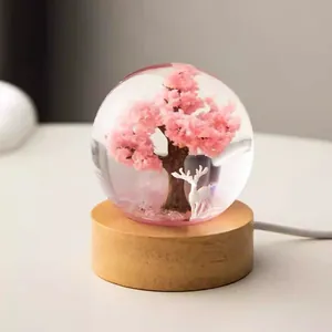 Detailed view of resin crystal ball night light with pink tree and deer on wooden base