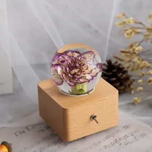 Detailansicht einer Kristallkugel-Spieluhr mit konservierter Blume und Holzsockel