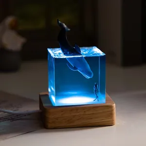 Detailed macro shot of a resin whale night light with a blue ocean glow and wood base.