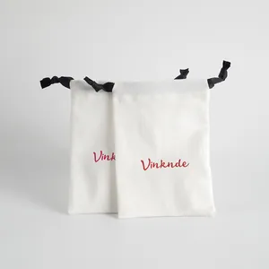 Detalle de bolsas para joyas blancas con cordones negros y logotipo de marca rojo.