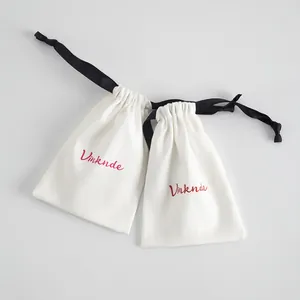 Vista detallada de bolsas de algodón blancas con cordón, logo rojo y cinta negra