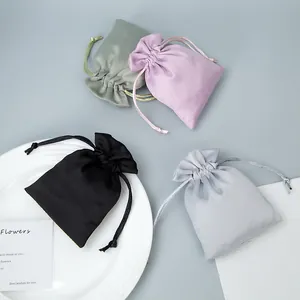 Four colorful satin drawstring pouches for jewelry storage on a white plate