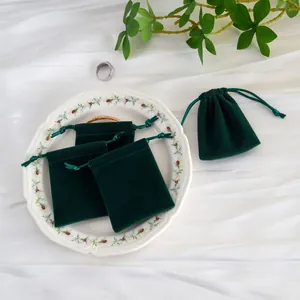 Detalle de bolsas de terciopelo verde oscuro con cordón para joyas en un plato