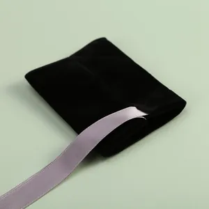 Gros plan d'un pochon à bijoux en velours noir avec un ruban lilas élégant.
