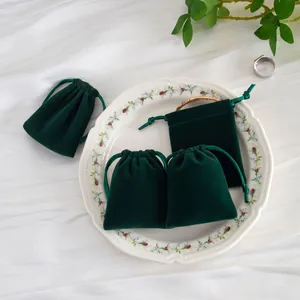 Elegantes bolsas de terciopelo verde oscuro con cordón para joyas en un plato blanco