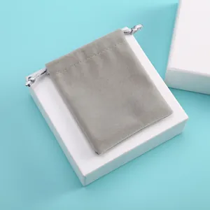 Gros plan d'un sac à cordon en velours gris pour bijoux sur une boîte blanche.