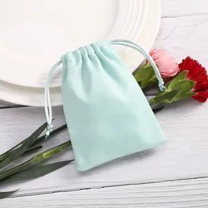 Bolsa de terciopelo verde menta con cordón para joyas sobre superficie de madera blanca