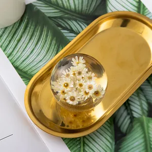 Elegant crystal ball with real dried daisy flowers on a golden decorative tray background.