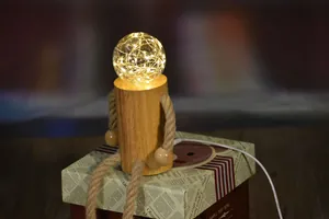 Dettaglio di una lampada notturna a forma di robot in legno su una scatola regalo.