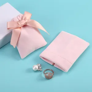 Gros plan de pochettes à bijoux en velours rose avec nœud sur fond bleu clair.