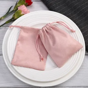Nahaufnahme von rosa Wildleder-Schmuckbeuteln mit Kordelzug auf eleganten Tellern.