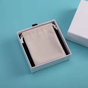 Detalle de una bolsa de terciopelo beige en una caja de regalo para joyas cuadrada blanca premium.