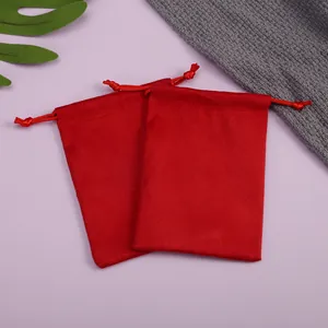 Detalle de dos bolsas de terciopelo rojo con cordón para joyas sobre fondo púrpura.