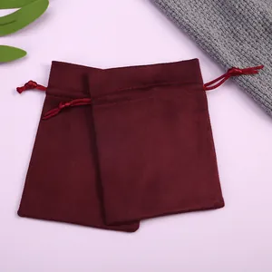 Detalle de bolsas de terciopelo rojo vino con cordón para joyas sobre fondo rosa