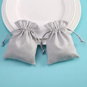 Vista detallada de dos bolsas de terciopelo gris con cordón para joyas sobre fondo azul