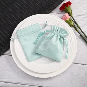 Detalle de bolsas de terciopelo verde menta para joyas en un plato blanco con flores.