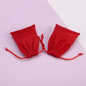 Dos bolsas de terciopelo rojo con cordón para joyas sobre un suave fondo pastel.