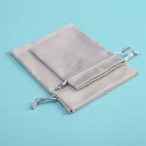 Detalle de dos bolsas de terciopelo gris con cordón para joyas sobre fondo azul.