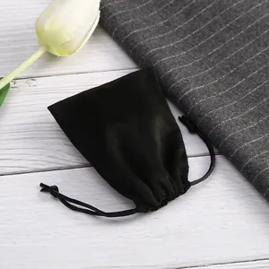 Detalle de una bolsa de ante negro con cordón para joyería sobre un fondo de madera blanca