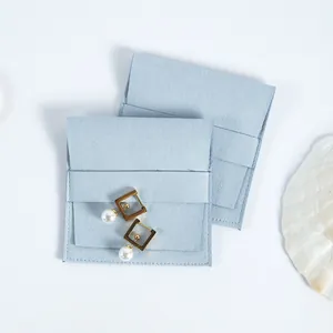 Detalle del sobre para joyas de microfibra azul claro con solapa y pendientes de perlas