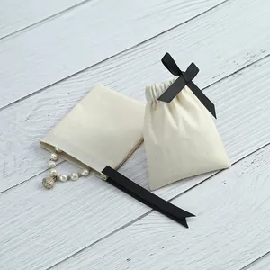 Détail de pochettes en coton écru avec ruban noir pour l'emballage de bijoux de luxe.
