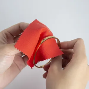 Detailed close-up of a red microfiber cloth cleaning a gold bracelet on white background.