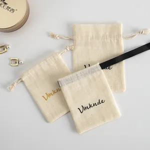 Détail rapproché de pochettes à bijoux en coton crème avec cordon et logo personnalisé.