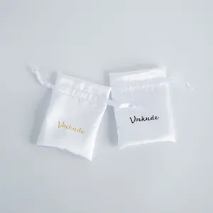 Close-up view of two white satin drawstring jewelry pouches featuring the Vinknde logo print
