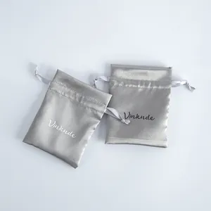 Primer plano de elegantes bolsas de satén plateado con textura suave y logotipo.
