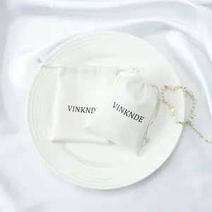 Detailed view of premium white silk drawstring pouches featuring the VINKNDE brand logo