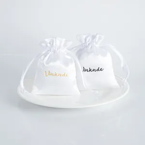 Close-up of two white imitation silk satin jewelry storage drawstring pouches on a plate