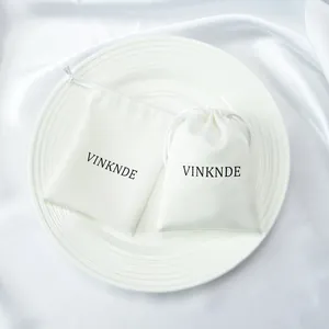 Detailed view of white microfiber drawstring pouches with brand logo on a white plate