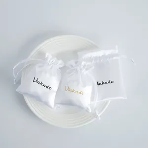 Group of three white satin drawstring jewelry storage pouches on a plate