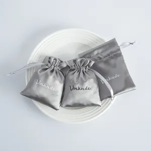 Bolsas de regalo de satén plateado con cordón sobre un plato blanco para joyas