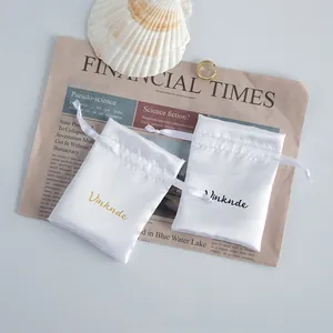 Detailed view of two white satin drawstring jewelry pouches on a vintage newspaper