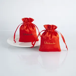 Close-up detail of two elegant red satin drawstring gift bags displayed on a white plate