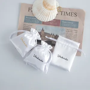 Detail shot of three elegant white satin drawstring jewelry pouches with silk-like texture.