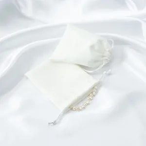 Close-up detail of white satin drawstring jewelry storage pouches on soft silk fabric