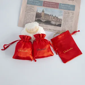 Three red satin drawstring gift pouches with Vinknde logo on lifestyle background.