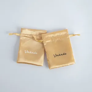 Close-up view of champagne satin drawstring jewelry pouches featuring printed Vinknde logo