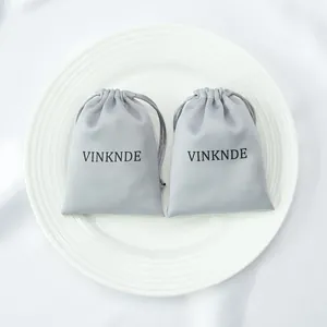 Close-up of two premium grey silk satin drawstring pouches with VINKNDE logo on a plate.