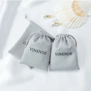 Detail view of grey satin drawstring storage bags with VINKNDE logo on white fabric