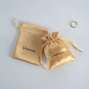 Close-up of gold satin drawstring bags for jewelry storage with black logo print