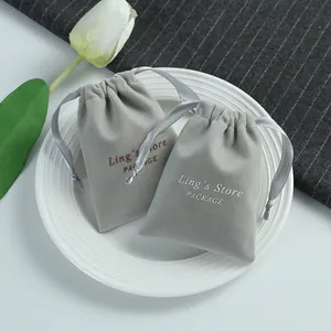 Detailed view of grey velvet drawstring jewelry pouches with logo on a white plate