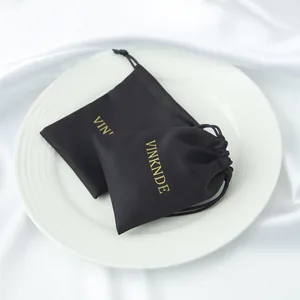 Primer plano de bolsas de regalo de satén negro con logotipo dorado en plato blanco