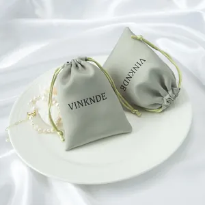 Gros plan de sacs cadeaux élégants en satin vert gris avec logo sur une assiette blanche.