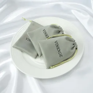 Gros plan de pochettes cadeaux en satin vert sauge avec cordon sur assiette blanche.