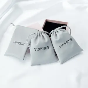 Close-up of three grey silky satin drawstring storage pouches with brand logo printed