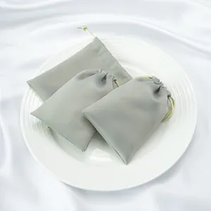 Gros plan de trois élégants sacs de rangement en satin gris avec cordon sur une assiette
